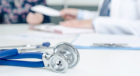 Stethoscope on a desk in front of a clinician with a patient faded in the background